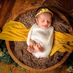A cozy baby wrapped snugly in a wooden bowl. The combination of the soft white wrap, the textured fur, and the pop of yellow fabric creates a beautiful, rustic portrait.