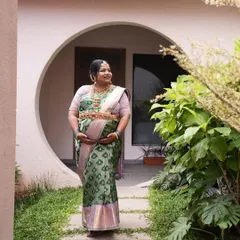 Pavithra walking through a garden, the soft light highlighting the gentle sheen of her silk saree. This is elegance perfected for a Seemantham ceremony.
