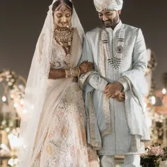 A gentle moment between the bride and groom. Her arm linked through his, they share a quiet, downward glance, a picture of serene togetherness amidst the wedding festivities.