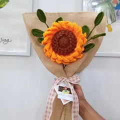 This is a single, large, handcrafted sunflower with green leaves, presented in a rustic burlap wrap tied with a gingham ribbon. It makes for a cheerful and timeless gift.