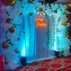 Another view of our nature-themed birthday arch, showing how the elements work together. The white drapes, green ivy, and warm neon light create a soft and inviting photo corner for your event.