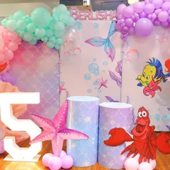 We transformed our space into an underwater paradise for this "The Little Mermaid" party. The decor features Ariel, Flounder, and Sebastian, along with a giant seashell and a marquee number '5'.