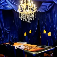 Another view of the casino-themed setup, highlighting the rich blue fabric and the warm glow of the chandelier and candles.