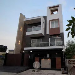 A full view of a modern residence elevation. The design plays with geometric forms, contrasting white planes with textured stone walls and warm wood accents to create a balanced and dynamic facade.