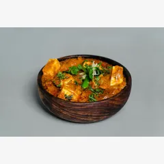 A wooden bowl of paneer butter masala, shot against a clean, neutral grey background. This is a standard product-on-white (POW) style shot, essential for any online menu.