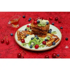 A wider view of the French toast platter, showing the full arrangement of fruit against a bold red background. This shot highlights the art of food presentation and plating.
