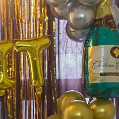 A close-up showing the fun details of a party backdrop. This image highlights a large champagne bottle foil balloon next to a gold and silver balloon garland, adding a celebratory element to the birthday decor.