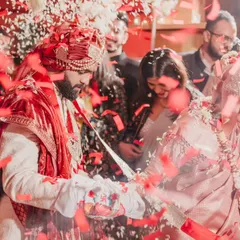 The couple taking their seven steps together, surrounded by the love and blessings of their family. The red confetti creates a vibrant and celebratory mood.