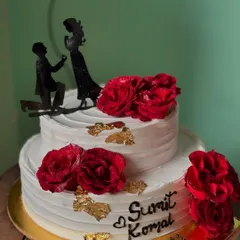 A romantic two-tier chocolate cake for an engagement. It's decorated with fresh red roses, gold leaf, and a silhouette topper of a proposal.