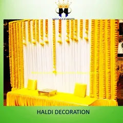 A simple yet elegant Haldi backdrop perfect for any space. This design uses a combination of white and yellow pleated drapes, with vertical strings of marigold flowers creating a classic and bright setting for the ceremony.