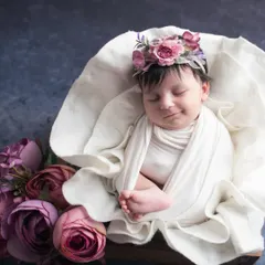 The same sweet girl, now peacefully asleep. This photo showcases the classic, serene newborn portrait, with the baby looking angelic and content, surrounded by soft flowers.