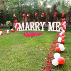 Agar aap kisi ko propose karna chahte hain, toh hum uske liye bhi special outdoor setup taiyar karte hain. Yeh 'MARRY ME' light letters, red aur white balloons, aur gulab ki pankhudiyon se sajaya gaya ek perfect proposal decoration hai.