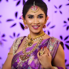 A close-up of a bride in a purple silk saree, showing how the drape complements the layered necklaces and maang tikka. Perfect draping ensures your jewellery takes centre stage.