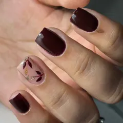 A subtle and luxurious design on short nails. This set features a dark brown polish with a nude accent nail, adorned with delicate, hand-painted leaves and a touch of glitter for an elegant finish.