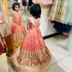 That mirror-check moment. She's admiring her custom peach and gold brocade frock, and honestly, I can't blame her. The pleated skirt and detailed border are designed for maximum impact.