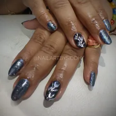 A dark, glittery cat-eye polish with a silver leaf-like design on the accent nail for a touch of mystery.