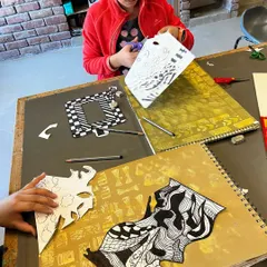 A student carefully cuts out intricate black and white patterns for a monochromatic still life project. This exercise focuses on form, pattern, and composition.