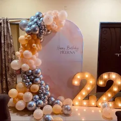 A stylish 22nd birthday decoration for Prerna. This home setup features an arched backdrop, a balloon garland in peach and silver, and large light-up marquee numbers.
