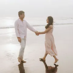 Ritu and Tarush holding hands as they walk along the shoreline. The soft sunset light and their reflections in the wet sand create a dreamy, romantic atmosphere for this pre-wedding photograph.