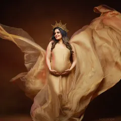 A powerful and angelic portrait using a golden gown and a sunburst crown. The flowing fabric creates beautiful wings, symbolizing the protective nature of a mother.