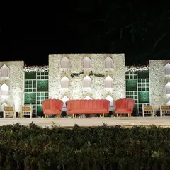 For a grand and earthy feel, we constructed this wide wedding stage using stone-textured panels and integrated green walls. The warm lighting in the jharokha-style niches and the blush-colored seating add a touch of modern elegance.