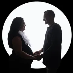 A sweet couple's silhouette against a circular light source, reminiscent of a full moon. Their happy expressions are just visible, adding a personal touch to the artistic shot.