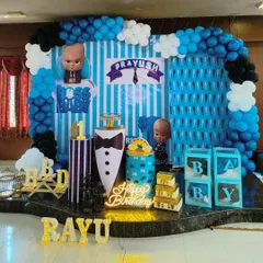 A detailed and exciting Boss Baby themed first birthday party. This setup includes a custom-printed backdrop, character cutouts, a balloon arch in theme colors, and personalized marquee letters spelling out the birthday boy's name.