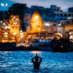 A lone devotee performs 'surya namaskar' in the holy Ganga at dawn, with the ancient city of Varanasi glowing in the background. This single frame captures the essence of faith and timelessness.