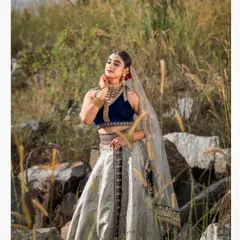 An outdoor bridal shoot capturing a serene and elegant moment. The natural setting complements the traditional lehenga, and the soft lighting highlights the delicate details of the fabric and embroidery.