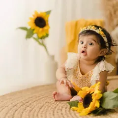A curious baby girl during her sitter session, looking with wide eyes at a sunflower. These milestone shoots are perfect for capturing their budding personalities.