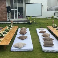 An outdoor movie night setup on a spacious lawn. We arranged low seating with mattresses and cushions in front of a large projector screen for a comfortable viewing experience.