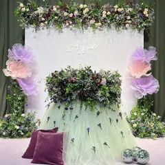 For baby Ayzah's cradle ceremony, we designed this breathtaking floral masterpiece. The decor features a custom tulle skirt for the main table, overflowing with fresh purple and lilac flowers, set against a clean white backdrop with a personalized name sign.