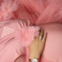 A beautiful detail shot focusing on the hand resting on the baby bump, showcasing the engagement ring and watch, all against the lovely texture of a pink ruffled gown.