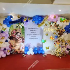 A traditional baby shower or naming ceremony setup with a Krishna-themed backdrop and an "Oh Baby" neon sign.