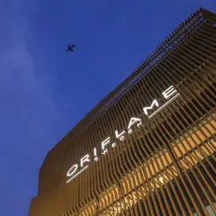 A dramatic low-angle shot of the Oriflame office facade against the evening sky. The illuminated signage and the texture of the slatted aluminum structure create a powerful brand statement.