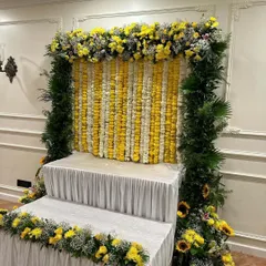 This is a classic and traditional Ganpati backdrop we prepared. It features alternating vertical garlands of yellow and white marigolds, framed by a border of fresh green leaves and yellow chrysanthemums.