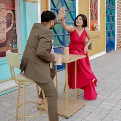 A playful moment sharing a drink against a vibrant blue door, reminiscent of a European street. The woman's bright red dress pops against the cool tones, creating a lively and stylish pre-wedding photo.