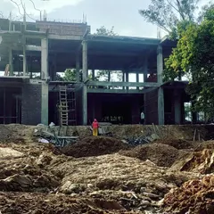 A wide view of the farmhouse construction site, showing the concrete frame and initial brickwork. The scale of the project is designed to be substantial yet respectful of the surrounding natural environment.