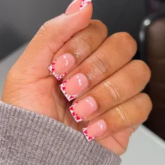 This design features a crisp white French tip decorated with a pattern of tiny red hearts. It's a bold and graphic look on a modern square nail shape.