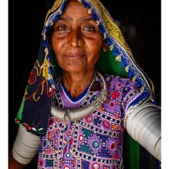A striking portrait of a Meghwal woman from Kutch, Gujarat. Her face is framed by her colorful, embroidered headscarf, and her traditional silver necklace and armbands complete the look.