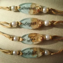 This set of custom name rakhis features a beautiful pastel blue background inside the resin. The names Sagar, Jai, and Ankit are written in an elegant script, complemented by delicate flowers, making each piece special.