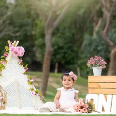 A beautiful outdoor portrait session featuring a pink floral theme with a teepee, perfect for a sunny day in the park.