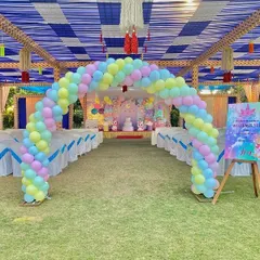 A grand unicorn party entrance in an outdoor setting. A pastel rainbow balloon arch welcomes guests to the celebration, with a themed welcome sign on an easel.