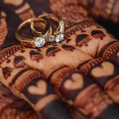 A close-up shot showcasing the rich, dark stain of the henna, beautifully complementing the couple's engagement rings. The heart details on the fingers are a sweet touch.