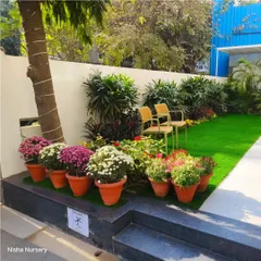 A cozy seating corner in a garden, featuring potted chrysanthemums on a raised platform next to a neat patch of artificial grass.