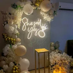 A beautiful "She Said Yes" backdrop ready for the big question. We used an elegant arched panel, a custom neon sign, and a lush arrangement of white, cream, and gold balloons with faux florals and candles to create a romantic setting.
