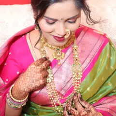 A bride admiring her beautiful layered Maharashtrian necklaces. The combination of a short choker and a long, elaborate haar creates a rich and authentic look.