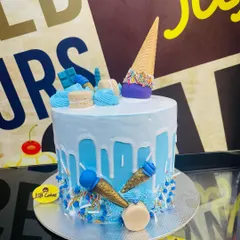 This light blue drip cake is decorated with an upside-down ice cream cone, macarons, and smaller edible cone details. The base is sprinkled with blue and white nonpareils, creating a fun and festive look for any birthday.
