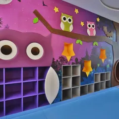 A nocturnal forest-themed room with a large owl-shaped bookshelf and star-shaped lights. The design uses a darker, calming palette to create a cozy and magical atmosphere for storytelling and quiet activities.