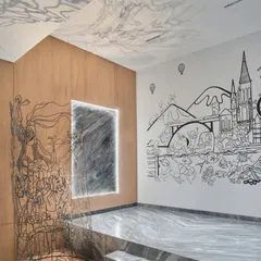 This monochrome mural is a surrealist travelogue, a memory reel of a family's adventures. The line illustration seamlessly transitions from the wall into a 3D metal sculpture, blending two-dimensional drawing with three-dimensional form to tell a continuous story.